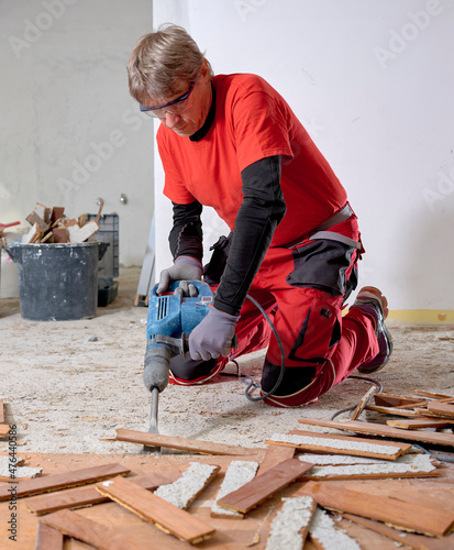 Wallpaper Mural Parquet in wood glued to the slab, removed with an electric demolition hammer by a craftsman in workwear, in the apartment under renovation. In the foreground, the removed parquet slats.  Torontodigital.ca
