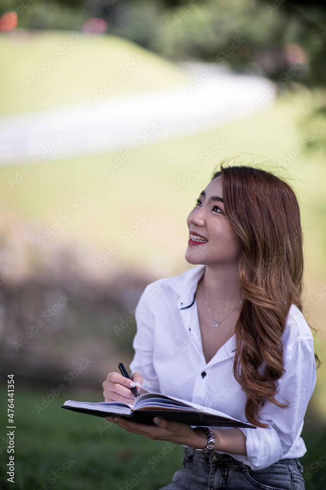 Obraz premium Joyful casual Asian student girl with laptop outdoors. Smiling woman sitting on the grass with a computer, surfing the net or preparing for exams. Technology, education and remote working concept