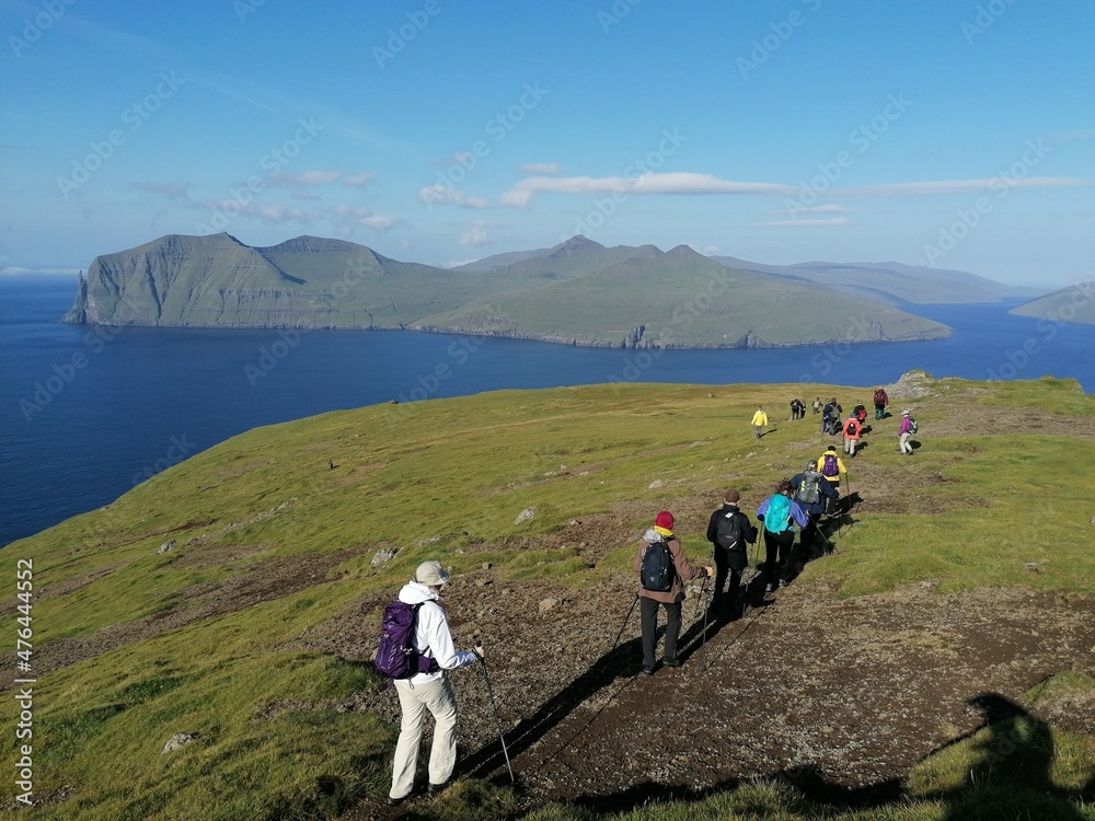 A group of hikers on a green mountain ridge walk in the Faroe Islands A group of hikers on a green mountain ridge walk in the Faroe Islands
