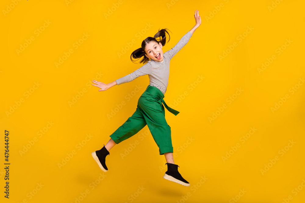 Full size profile side photo of young girl happy positive smile grimace tongue-out jump isolated over yellow color background