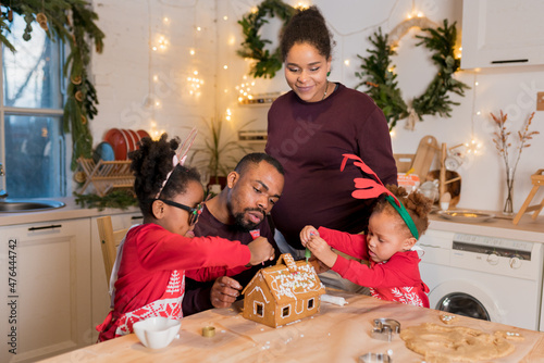 African American family decorating a gingerbread house together on Christmas day.  Christmas moments with kids at home concept