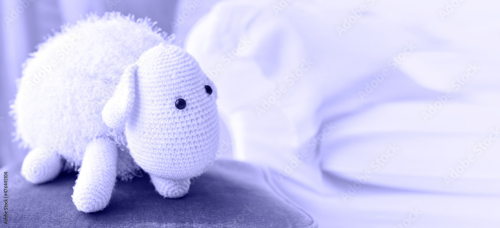 Knitted lamb from threads on velor chair painted in main trendy Very Peri color of year 2022. Lamb soft children's toy. Closeup. Soft focus.Banner. Copy space for text. Knitted lamb from threads on velor chair painted in main trendy Very Peri color of year 2022. Lamb soft children's toy. Closeup. Soft focus.Banner. Copy space for text.