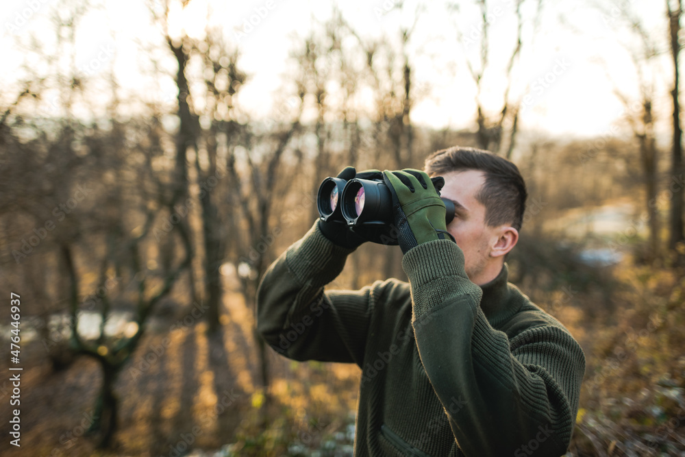 Professional hunter looking through binoculars. Man on the hunt in the middle of forest. Professional hunter looking through binoculars. Man on the hunt in the middle of forest.