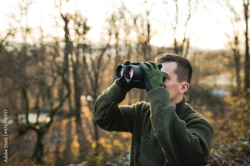 Professional hunter looking through binoculars. Man on the hunt in the middle of forest. 
