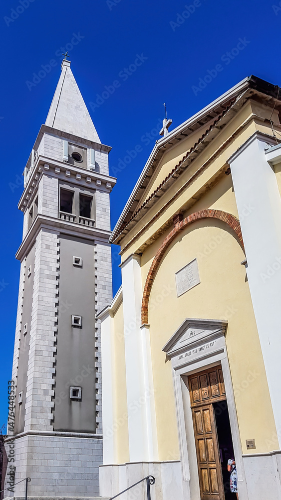 Obraz premium A view on a church and a bell tower from the bottom. The walls of the church are painted yellow, and bell tower's are painted grey. Buildings nicely contrasted with a clear blue sky.