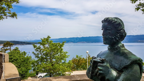 Vrbnik/Croatia-05/01/2018: A statue of a man, located at the top of a hill with a beautiful view on the sea. Some trees disturbing the view on the sea. Bench vith the sea view. photo