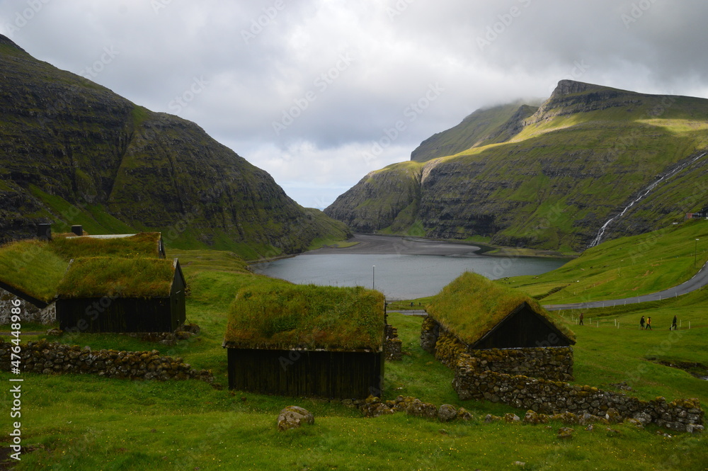 Cute old stone houses with grass roof overlooking the bay and green mountains on the Faroe Islands