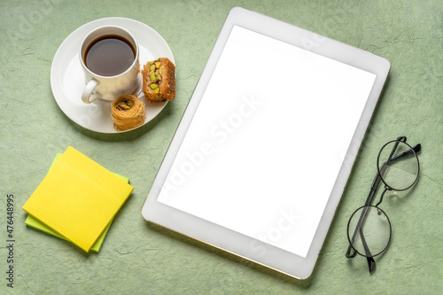 mockup of digital tablet with a blank isolated screen (clipping path included) with coffee, baklava, and reading glasses against handmade paper