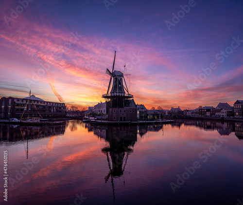 Beautiful sunrise with pink and orange clouds at the Adriaan windmill along the Spaarne river in Haarlem, reflected in the water