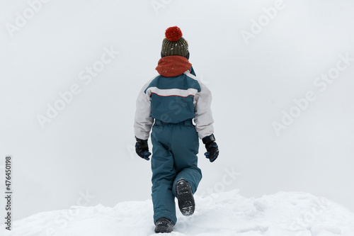 Back view the child walks in the winter on the street. Boy walks on loose snow. Cold winter day.