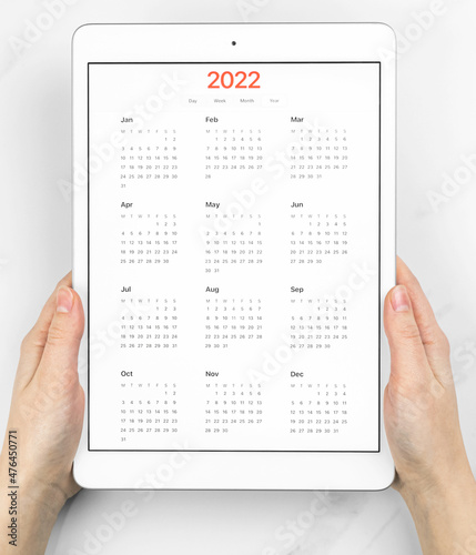 2022 calendar on screen, hands with tablet computer. White marble background. Concept photo of planning appointment and meeting