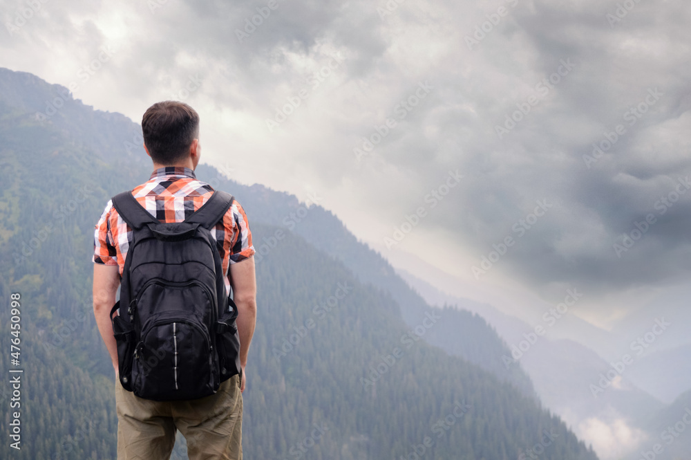 A tourist with a backpack stands alone in the mountains and sees a dark stormy sky. The concept of air pollution, environmental problems, the crisis of the tourism industry.