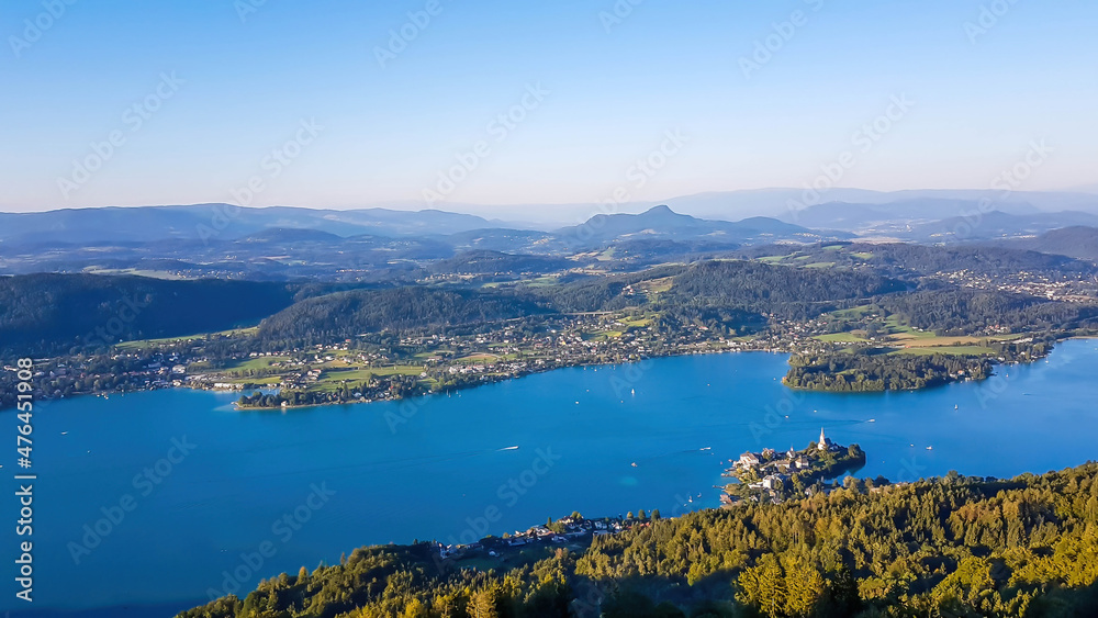 A view on the Woerthersee lake from the observation deck of Pyramidenkogel Tower. Lake is reflecting the last beams of sun for this day. Golden hour. The surrounding hills are shining gold.