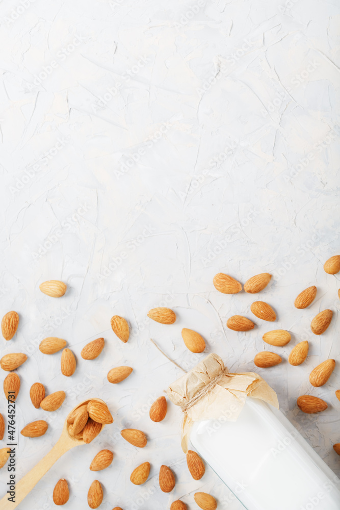 Almond milk in a glass bottle on a light background with a scattering of seed kernels and a wooden spoon. Almond milk in a glass bottle on a light background with a scattering of seed kernels and a wooden spoon.