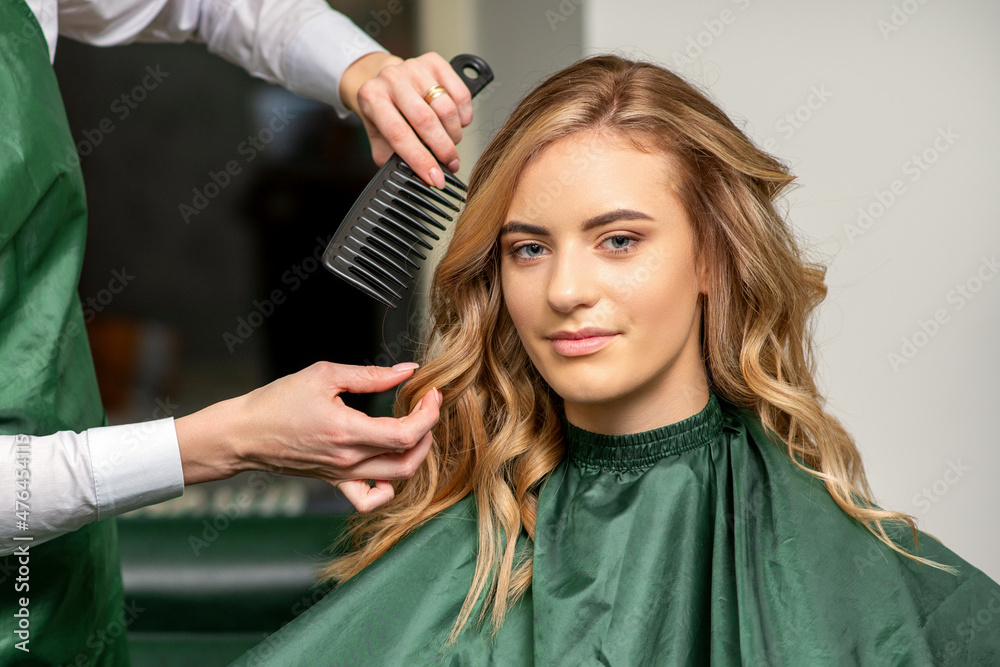 Fototapeta premium Hairdresser making hairstyling for the woman while combing with hairbrush, comb in a hair salon