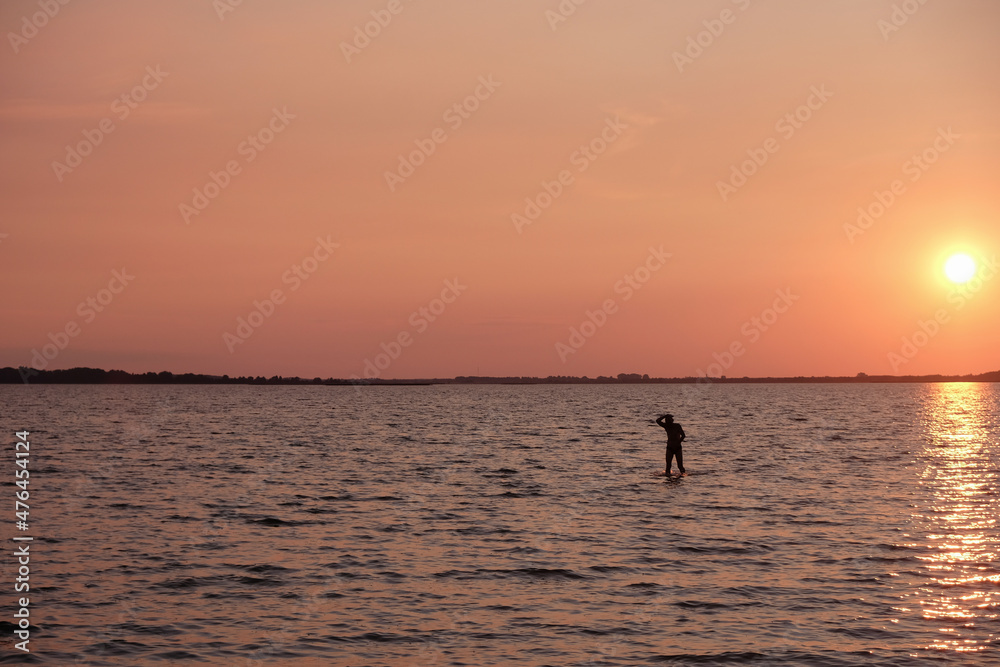 Silhouette of a lonely man in the water. Calming coral color sunset background. Svityaz lake, Ukraine. 