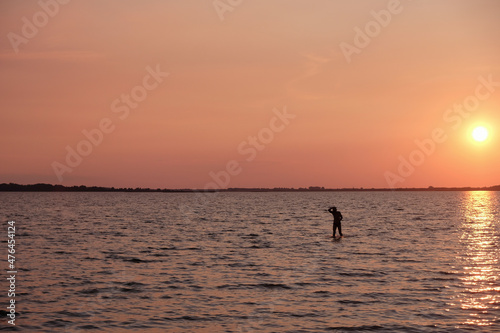 Silhouette of a lonely man in the water. Calming coral color sunset background. Svityaz lake, Ukraine.  © Ganna Zelinska