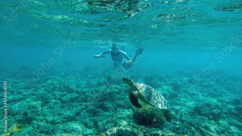 A girl in a diving mask and fins diving along a turtle, next to the shore of Gili Air, Lombok Indonesia. Beautiful and crystal clear water. Peaceful coexistence of human and animal. Dream coming true. © Chris