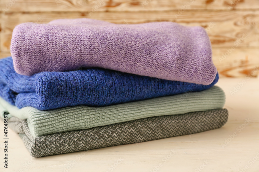 Stack of different cozy sweaters on light wooden background
