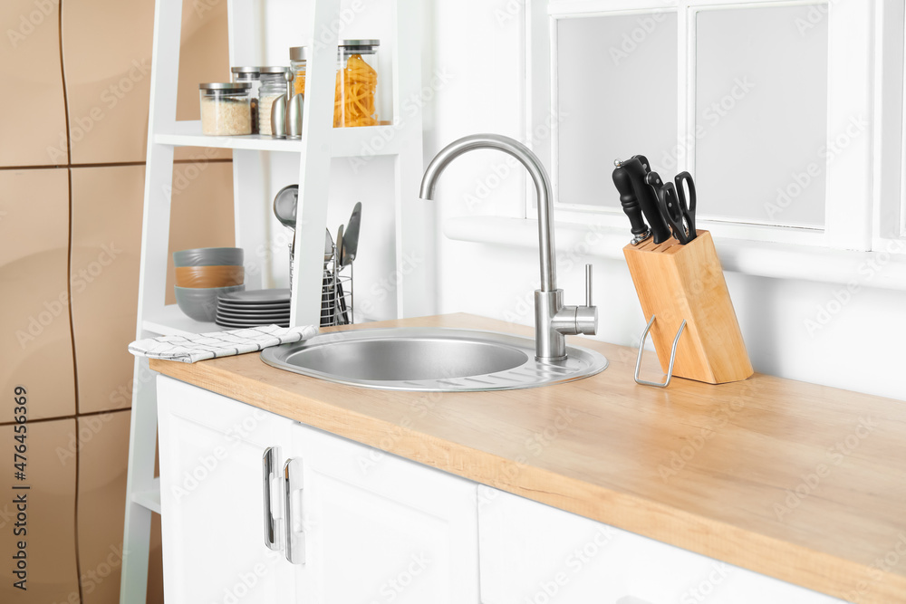 Fototapeta premium Wooden counter with silver sink and set of knives near window in kitchen