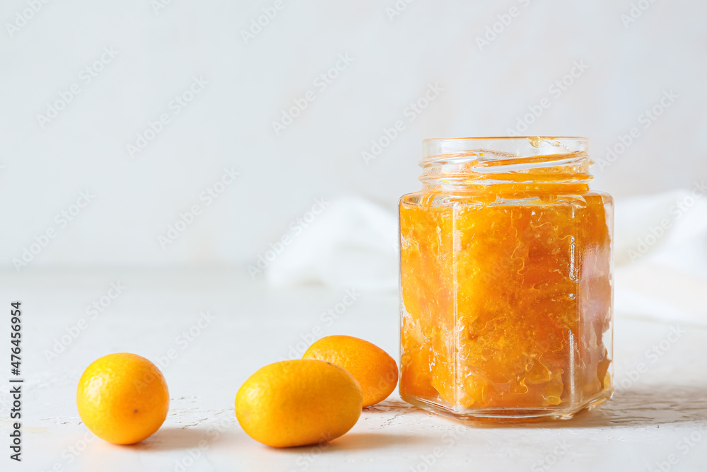 Jar of tasty kumquat jam and fresh fruits on light background Jar of tasty kumquat jam and fresh fruits on light background