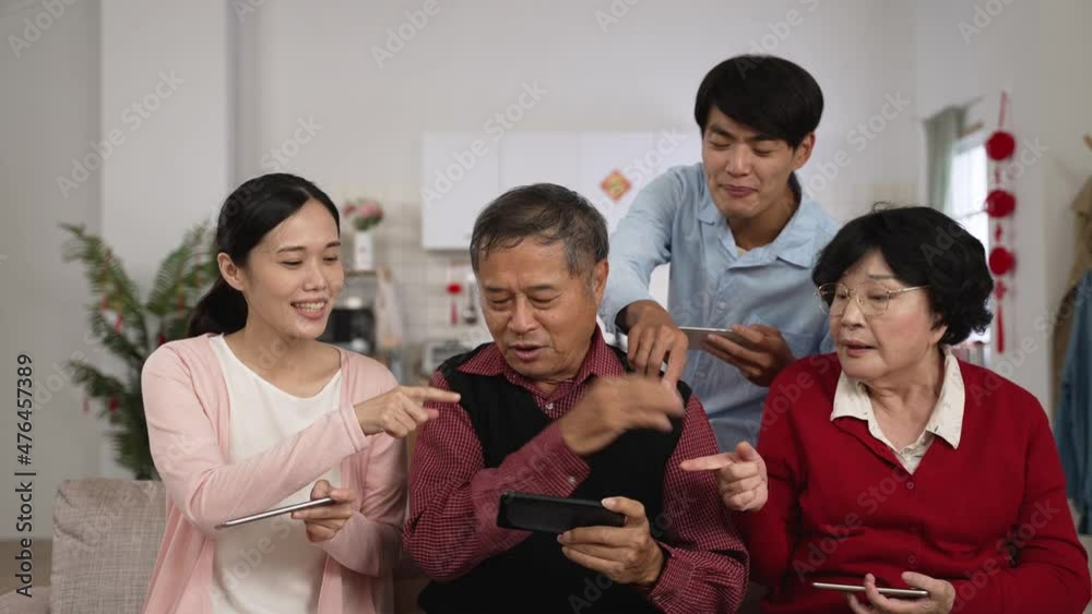 elderly father wearing red shirt playing mobile game is waving hands and feeling annoyed as other family members is pointing and nagging around him during spring festival at home elderly father wearing red shirt playing mobile game is waving hands and feeling annoyed as other family members is pointing and nagging around him during spring festival at home