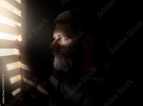 a man with a beard is hiding in the dark, only his eyes are illuminated through a crack from the window
