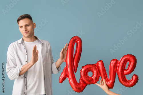 Displeased man refusing balloon in shape of word LOVE on color background photo