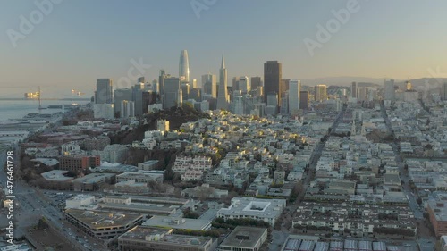 4K aerial video footage of San Francisco, California, at sunset. Movement is retreating towards Pier 39 area. Tops of buildings and houses lit by yellow by setting sun.