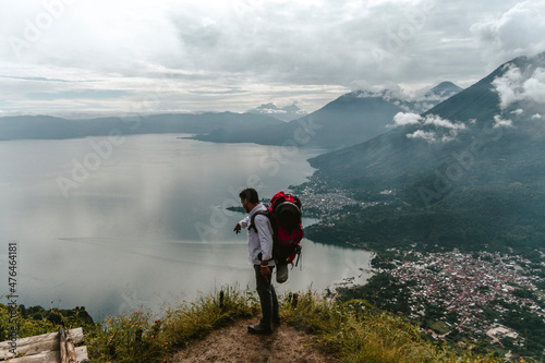 Hombre latino en la cima de una montaña con vista a un lago rodeado de volcanes