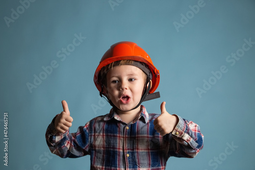 Portrait of adorable little child in a protective orange helmet showing thumb up