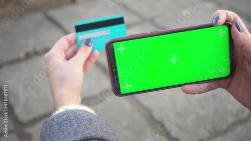 Smartphone and credit debit card in hands of girl smartphone green screen for chroma key on street in autumn. Internet commerce and payments for goods and services via Internet for online shopping 4k