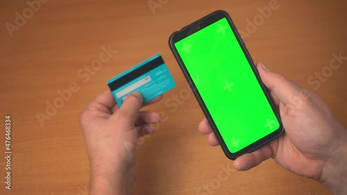 Smartphone and credit debit card in hands of man smartphone green screen for chroma key on street in autumn. Internet commerce and payments for goods and services via Internet for online shopping 4k
