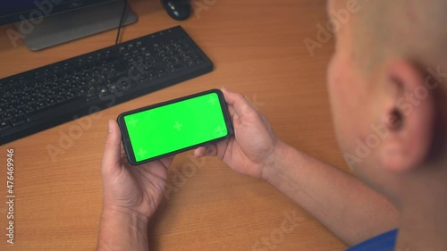 Top view of male hands holding mobile phone with green mock up screen. Caucasian man using modern smartphone at workplace. Surfing Internet Watching Content Videos Blogs Tapping on Center Screen 4k