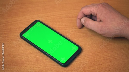 Top view of male hands holding mobile phone with green mock up screen. Caucasian man using modern smartphone at workplace. Surfing Internet Watching Content Videos Blogs Tapping on Center Screen 4k
