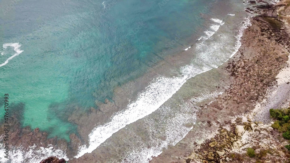Top-down drone shot of an idyllic Koka Beach. Hidden gem of Flores Indonesia. Beauty in the nature. Calm waves washing the cliff's slopes. Serenity and calmness. There are a lot of boulders in the sea