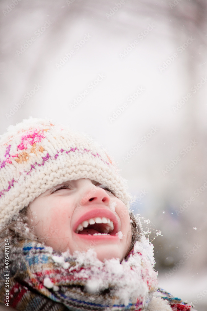 Girl smiling during a snowfall. Outdoors winter activities for kids. Cute child wearing a warm hat low over her eyes catching snowflakes with her mouth
