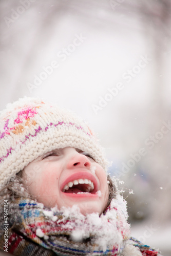 Girl smiling during a snowfall. Outdoors winter activities for kids. Cute child wearing a warm hat low over her eyes catching snowflakes with her mouth