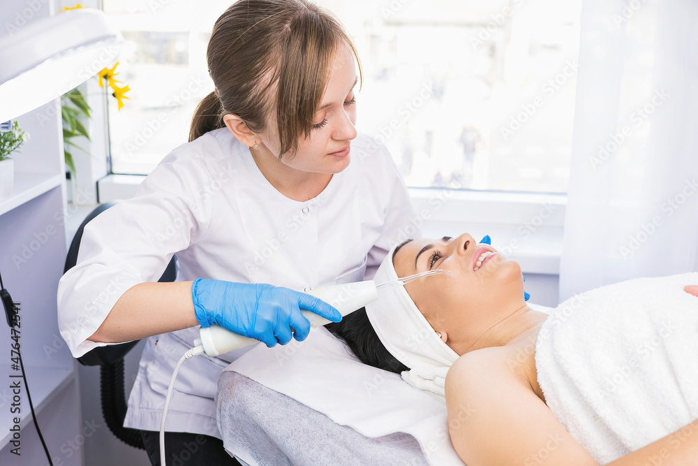 Cosmetologist makes procedure microdermabrasion on the face against acne to a woman, rejuvenation cosmetology concept. Cosmetologist makes procedure microdermabrasion on the face against acne to a woman, rejuvenation cosmetology concept.