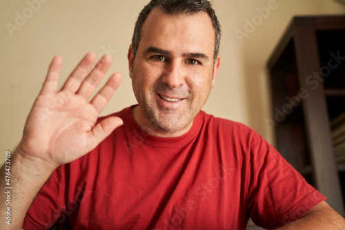 A friendly man waving during a video call, as seen on a device screen