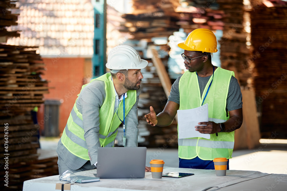 Black worker and warehouse inspector cooperate while going through distribution plans at storage department. Black worker and warehouse inspector cooperate while going through distribution plans at storage department.