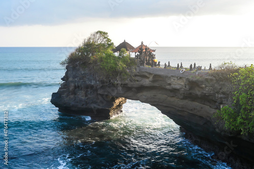 Cliffs in the nearby of Tanah Lot Temple, Bali, Indonesia. There is an arch in the water. The waves are splashing on the cliffs and smaller rocks. Water stays on the flat surfaces. Power of the nature