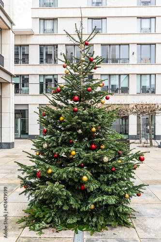 geschmückter Weihnachtsbaum im Freien vor einem Gebäude mit roten und goldenen Kugeln 