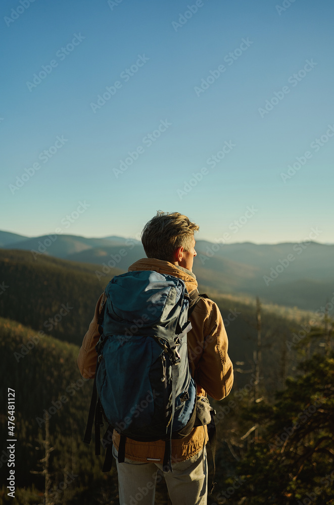 Nature view of mountains and hills with woods at sunset, back view man hiker admiring landscape, travel point destination