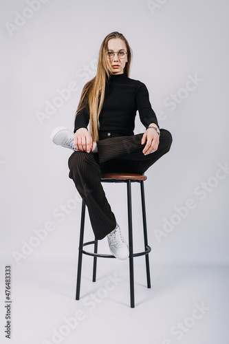 Studio candid unaltered portrait of young blonde woman with long hair sitting on chair. Portrait of Fashionable stylish blonde long hair girl in casual style cloth