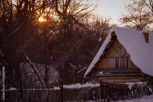 A house with a snow-covered roof in the village at dawn.