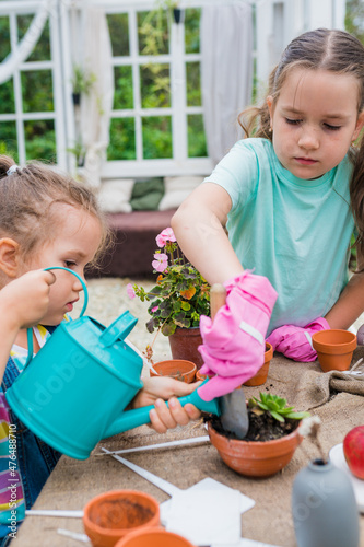 Gardening with kids. Girls taking care of plants in pots at greenhouse. Learning and activities for growing with children concept