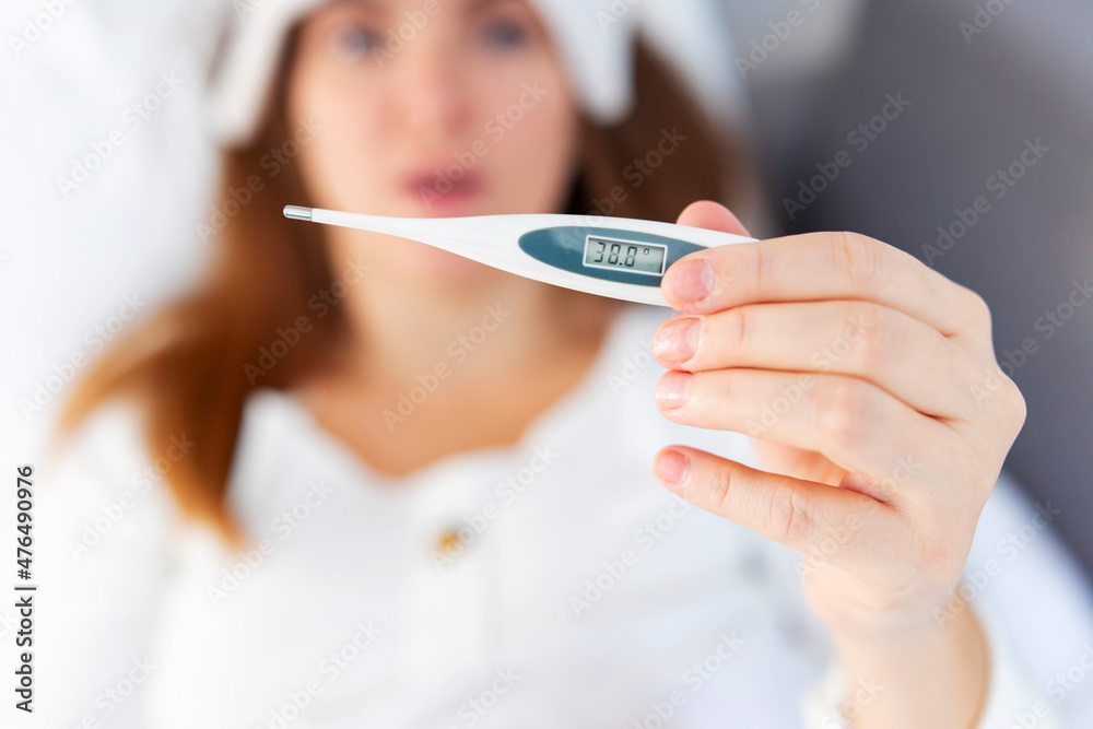 Closeup of womans hand with a medical thermometer with very high body temperature. Fever. Young sick woman checking her body temperature