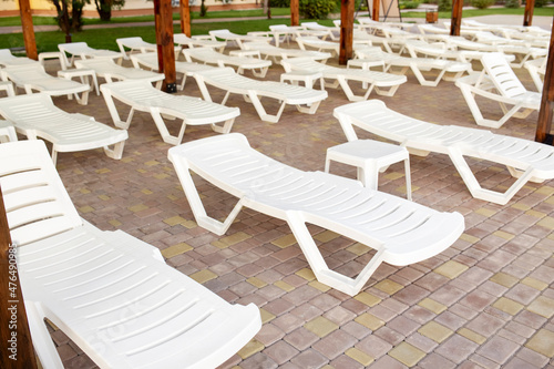 Empty white plastic loungers near the swimming pool on a summer day. Summer holidays and tourism. Relaxation area  place to rest