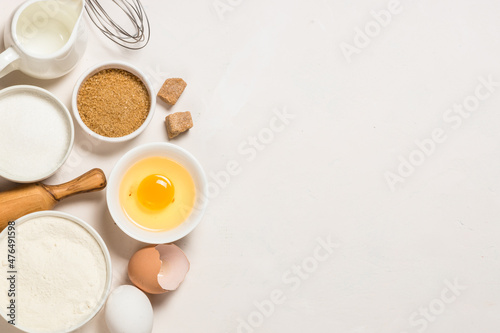 Baking ingredients at white table. Flour, sugar, eggs and utensils. Top view with copy space.